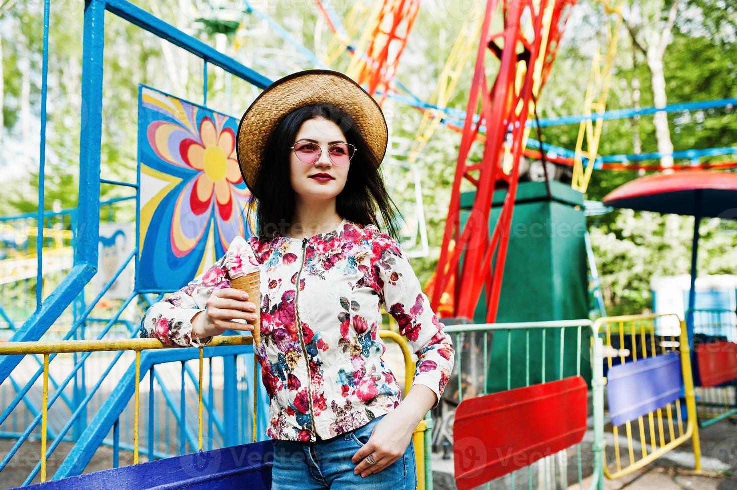 Portrait of brunette girl in pink glasses and hat with ice cream at amusement park. photo