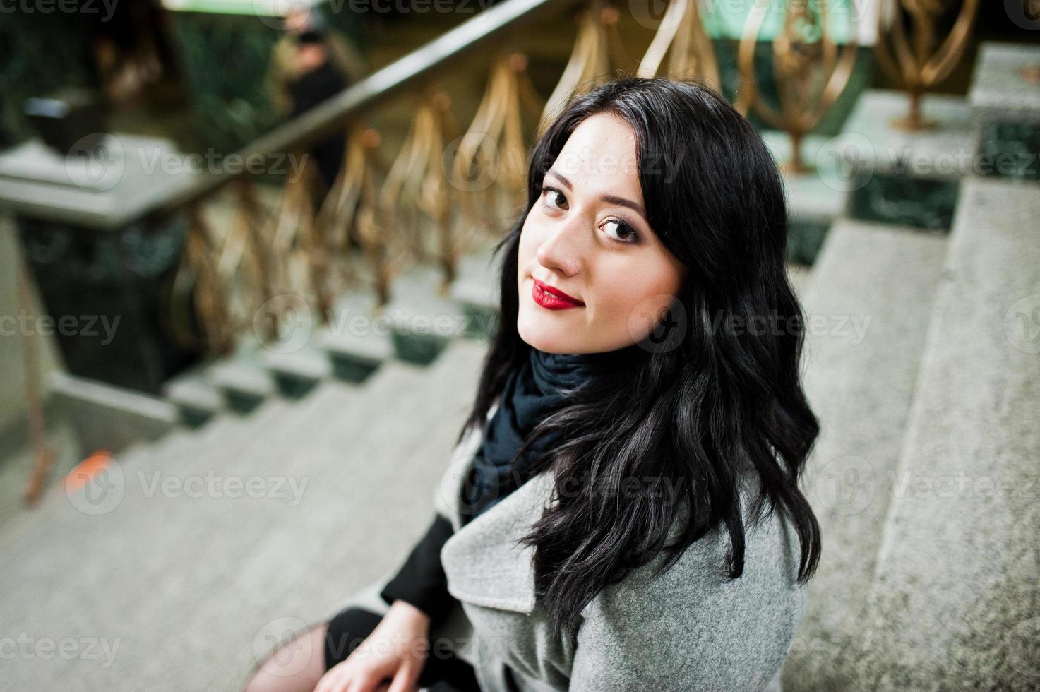 Brunette girl in gray coat posed in stairs of railway station indoor. photo