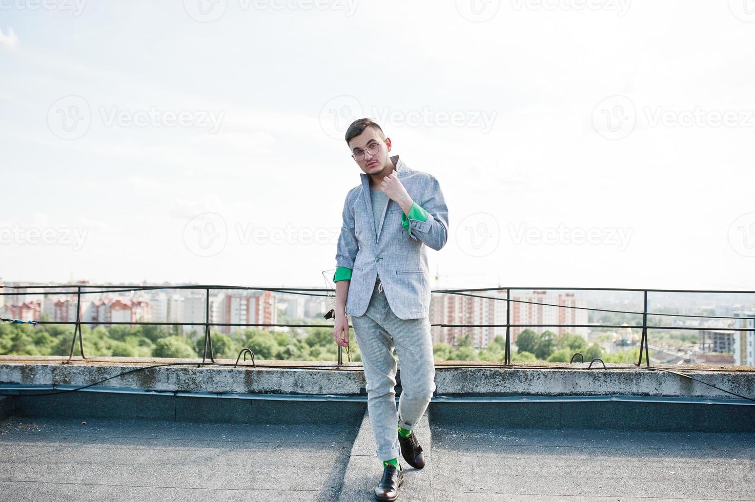 Dreamer stylish macho man in gray suit and glasses posed on the roof. photo