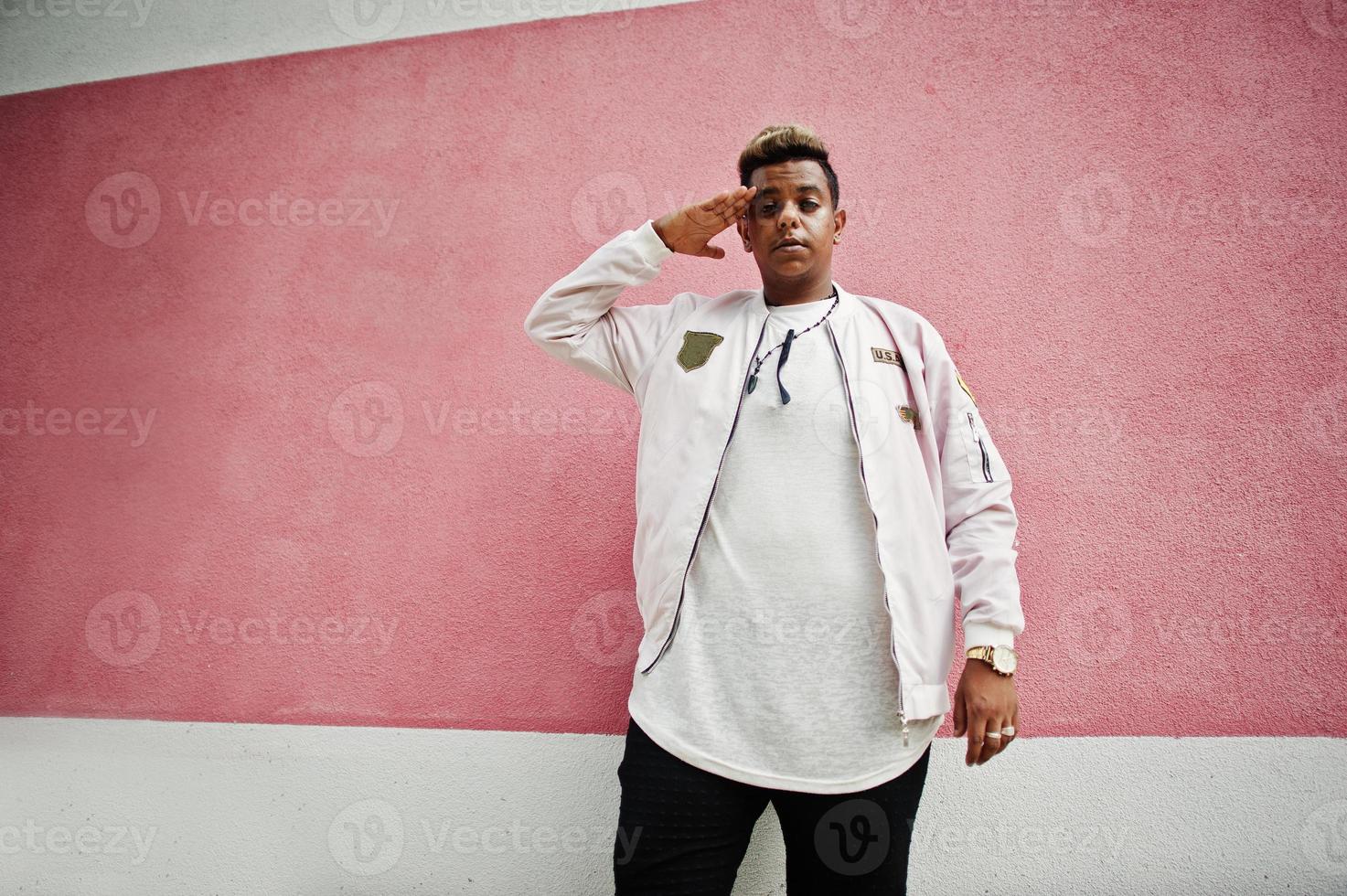 hombre árabe con estilo hipster posó al aire libre en la calle. cantante de rap de estilo contra la pared rosa. foto