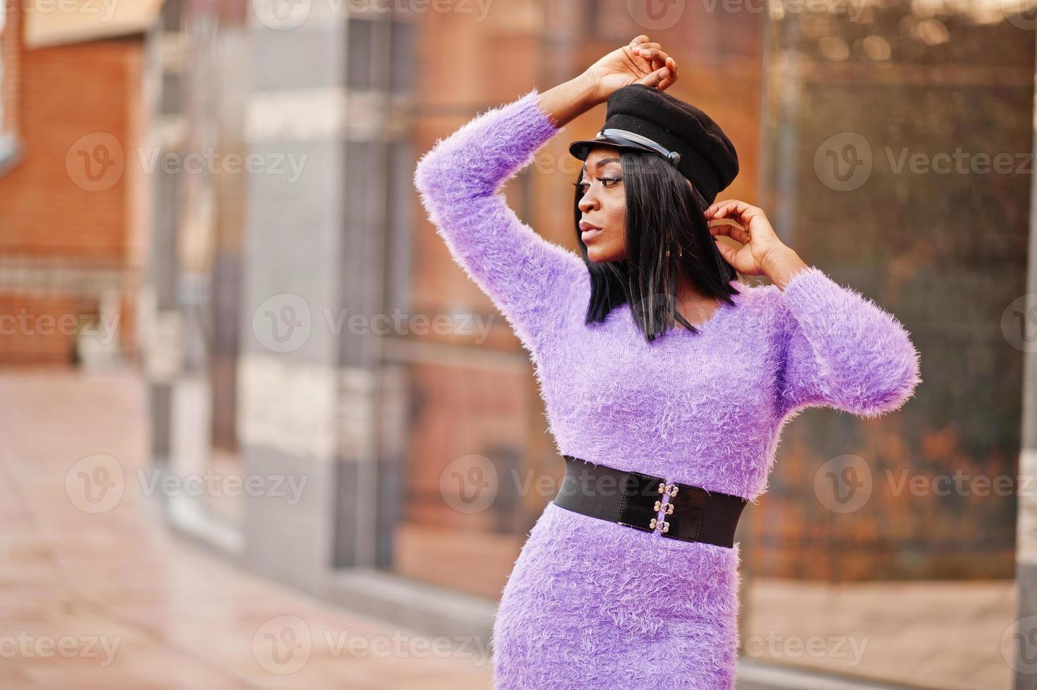 African american woman at violet dress and cap posed outdoor against modern building. photo