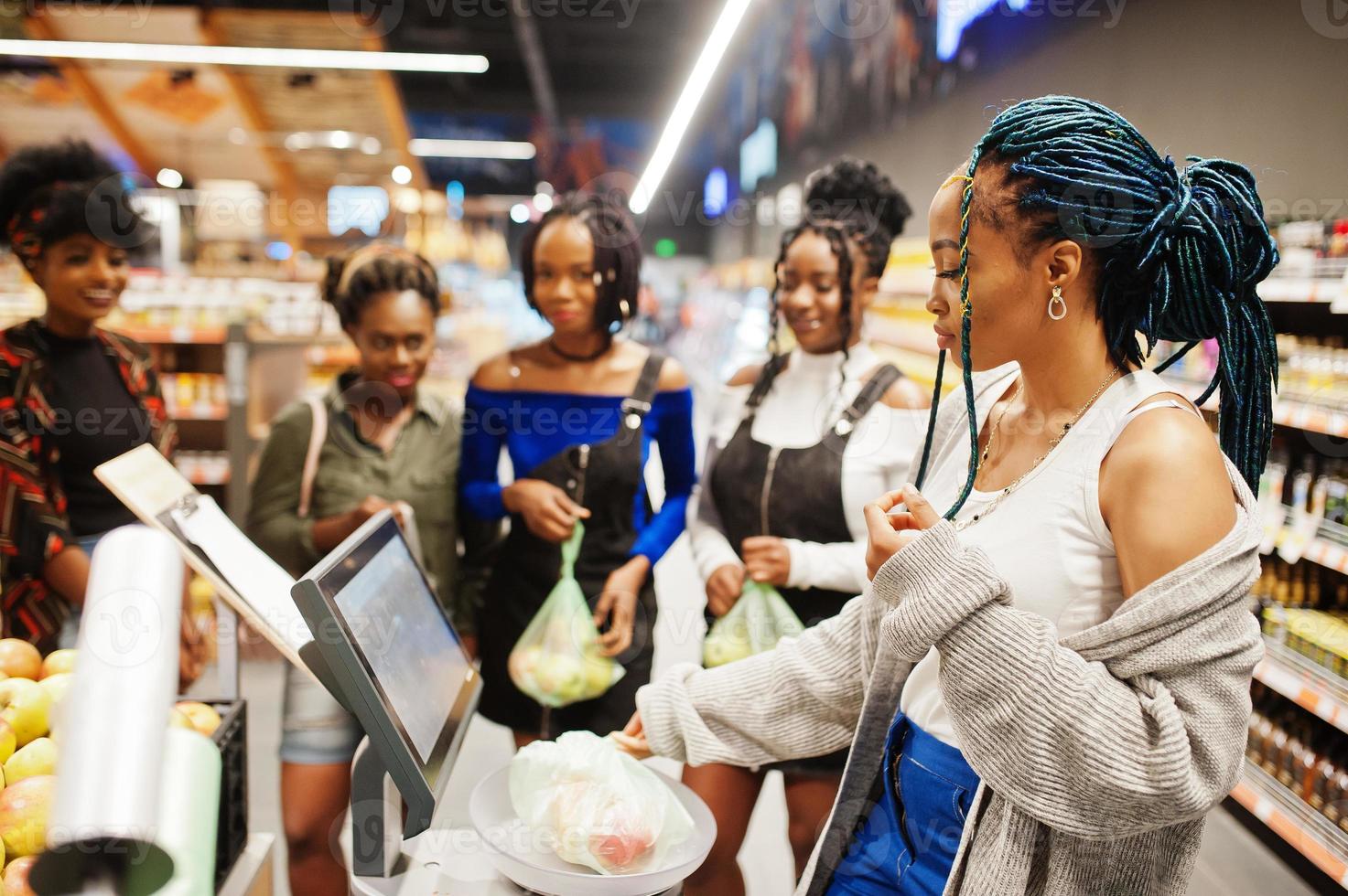 Group of african womans weighs apples in polyethylene bags at supermarket. photo