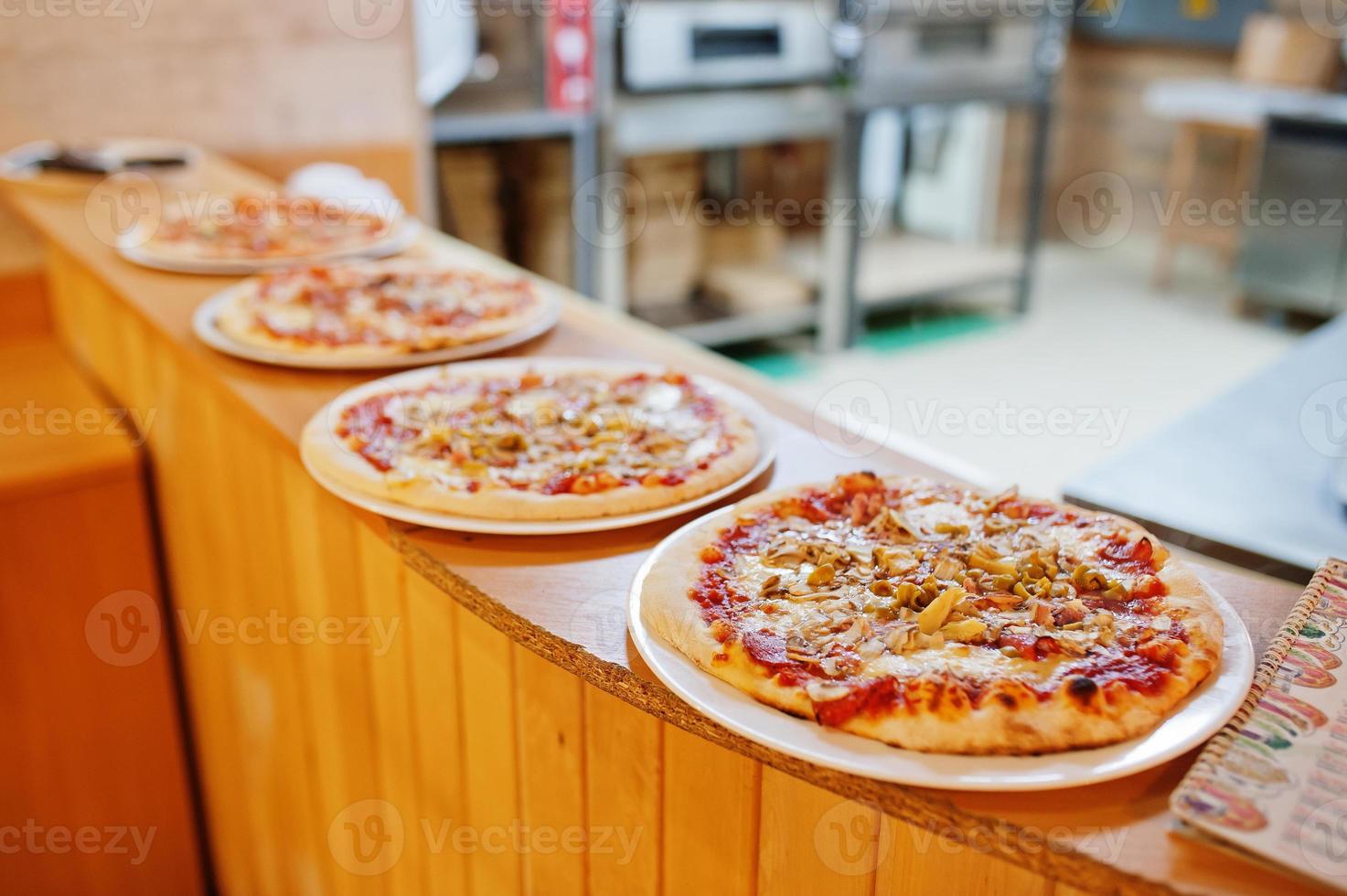 cuatro pizzas en la cocina del restaurante listas para ordenar. foto