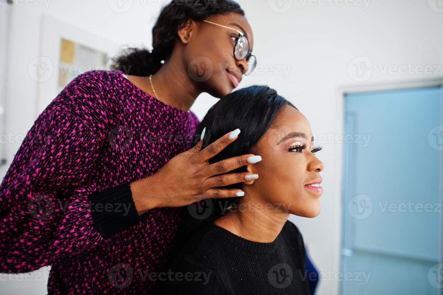 African American woman applying make-up by make-up artist at beauty saloon. photo