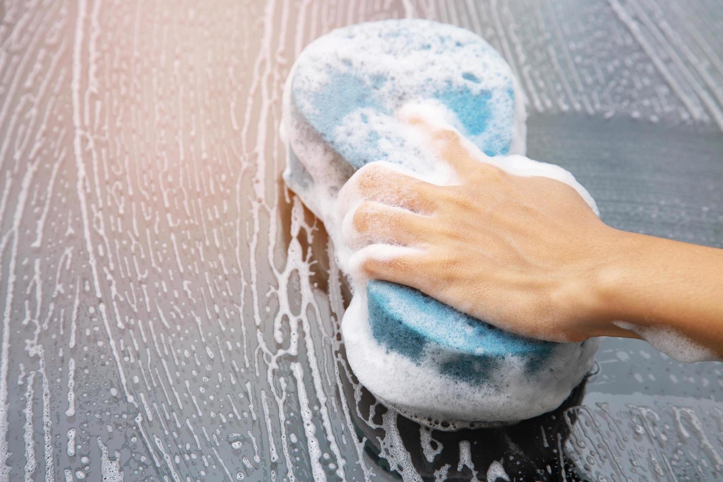 people worker man holding hand blue sponge and bubble foam cleanser window for washing car. photo