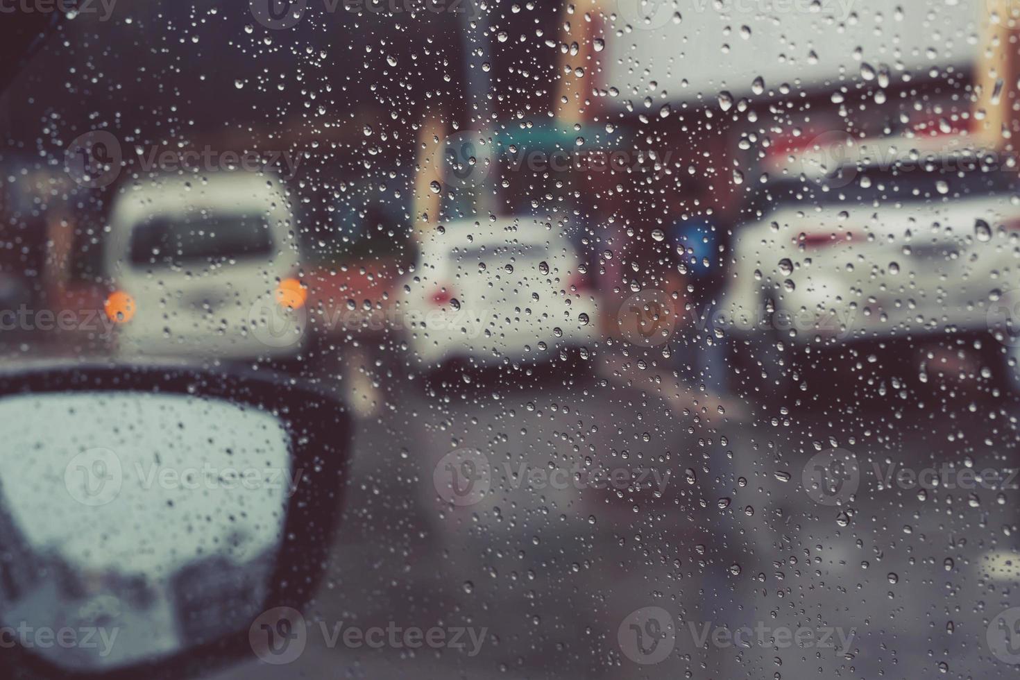 Drops Of Rain Drizzle on the glass windshield in the evening. street in the heavy rain. Bokeh Tail light and Traffic lights in city. Please drive  car carefully, slippery road. soft focus. photo