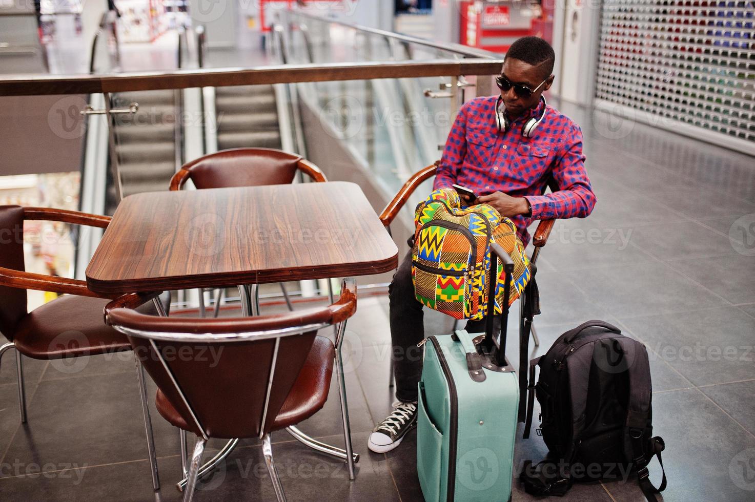 African american man in checkered shirt, sunglasses and jeans with suitcase and backpack. Black man traveler on duty free. photo