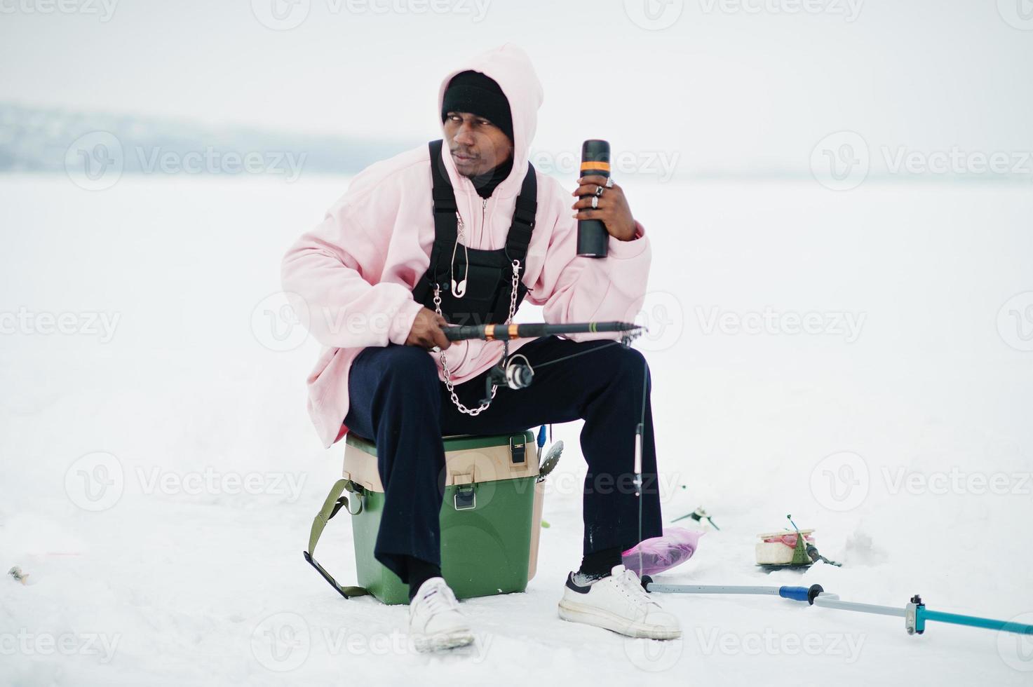 African american fisherman with fishing rod and thermos. Winter fishing. photo