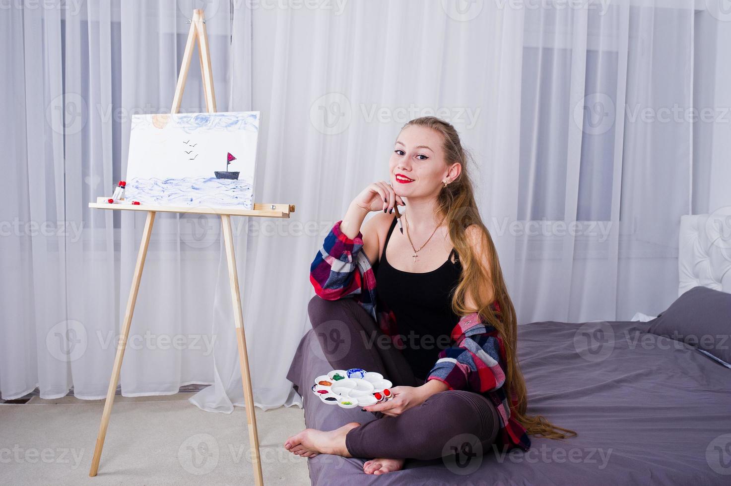 Beautiful woman artist painter with brushes and oil canvas posing bed at room. photo