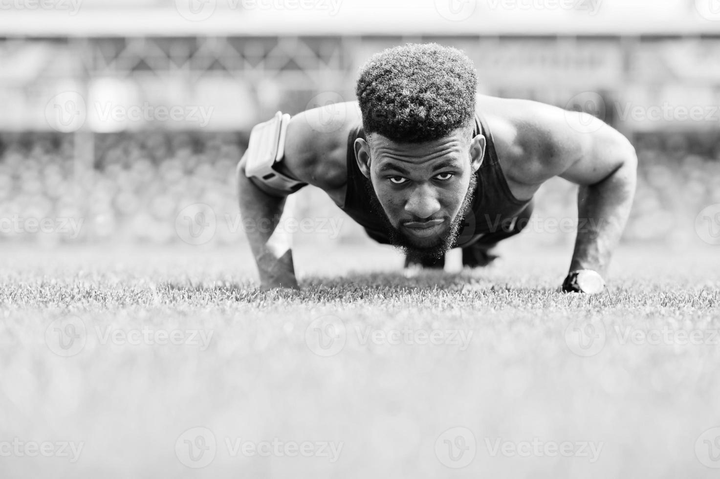 African american male athlete in sportswear doing push-up exercise at stadium. photo