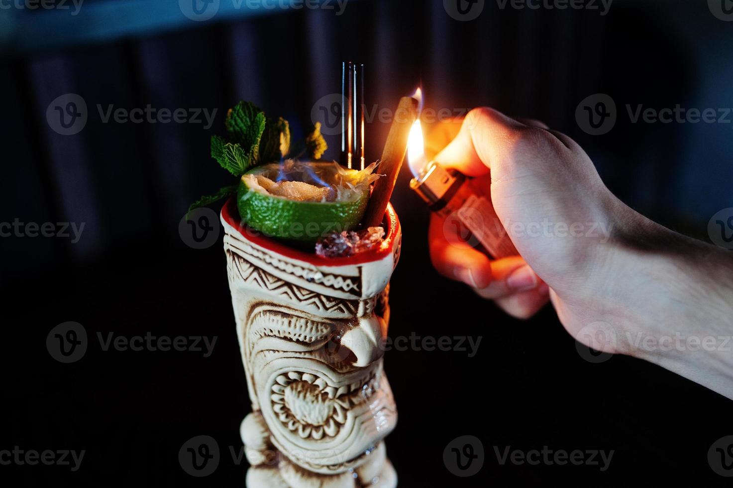 Alcoholic cocktail with mint and lime with fire in originally voodoo earthen glass on bar table. photo