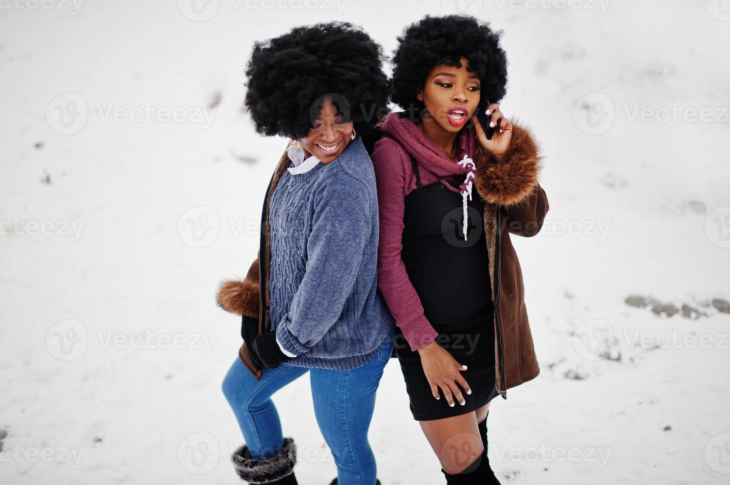 Two curly hair african american woman wear on sheepskin coat and gloves posed at winter day, speaking on phone. photo