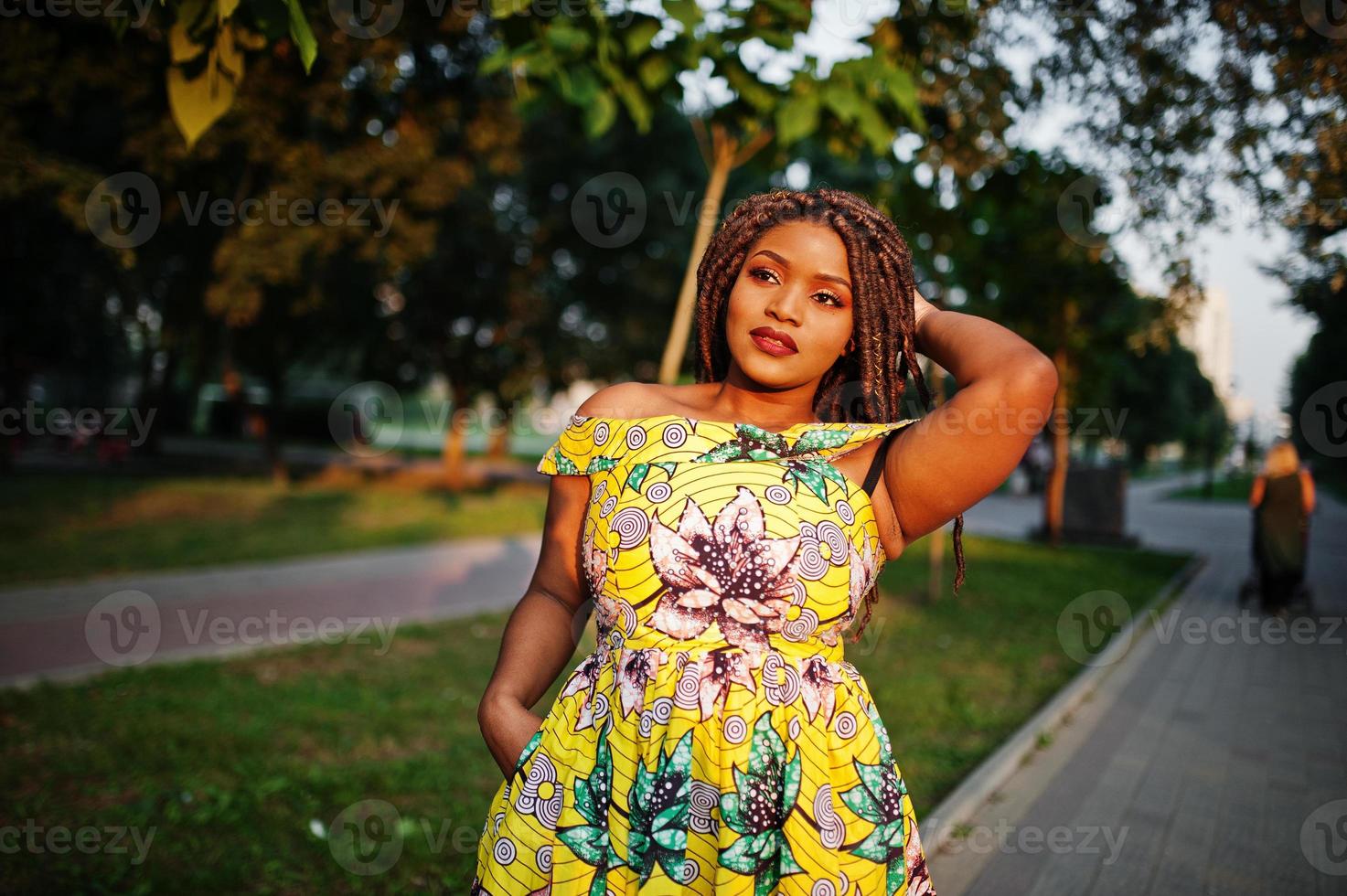 Cute small height african american girl with dreadlocks, wear at coloured yellow dress, posed at sunset. photo