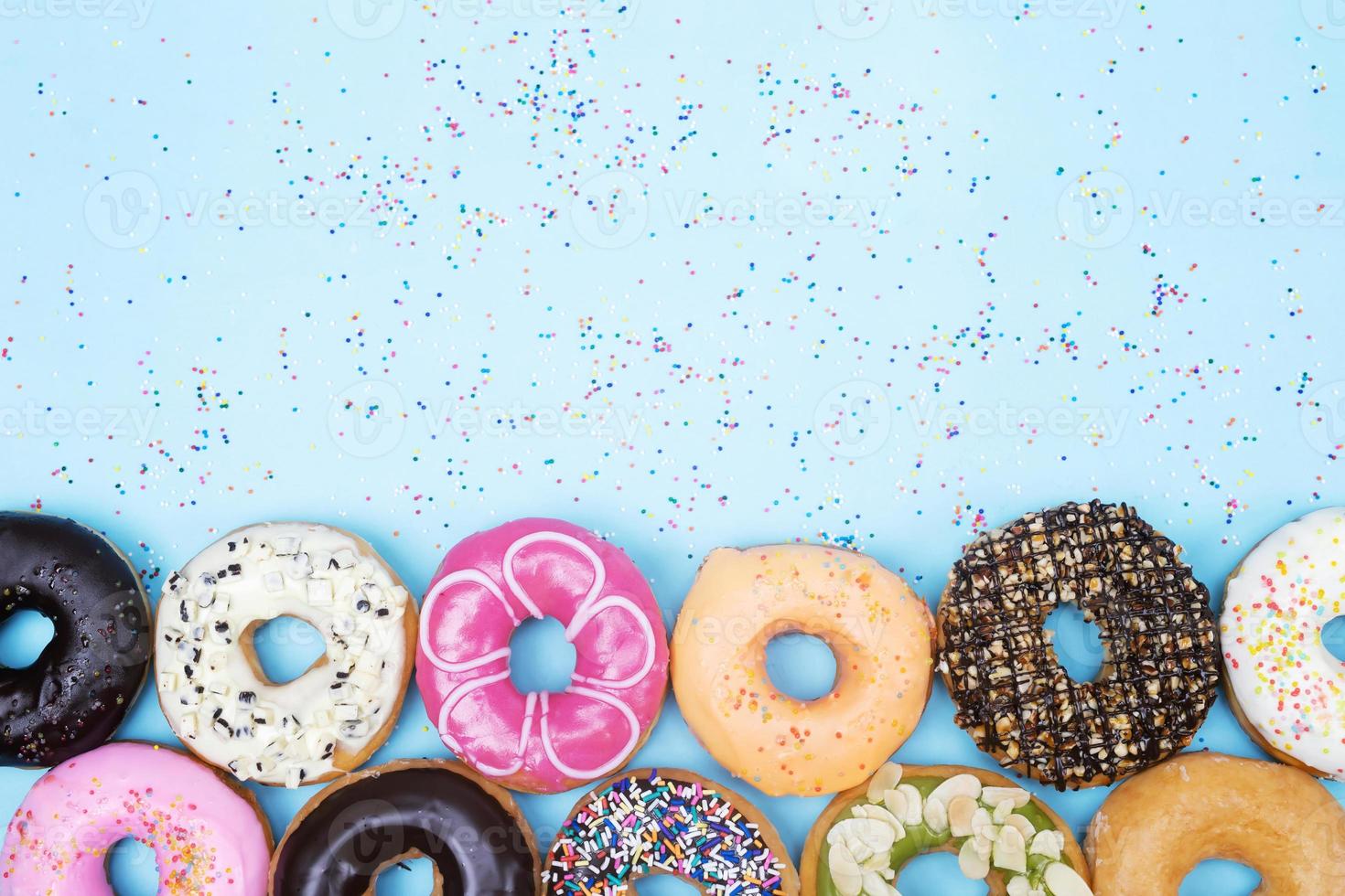 assorted donuts with chocolate frosting, topping sprinkles donuts Colorful variety and Variety of flavors mix of multi colored sweet donuts with frosted sprinkled on blue background. top view photo