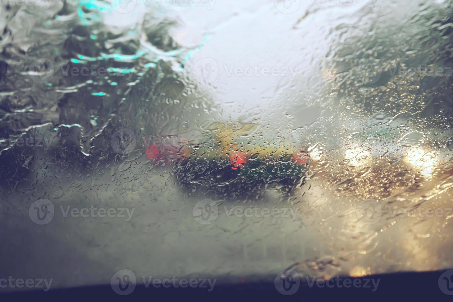 Drops Of Rain Drizzle on the glass windshield in the evening. street in the heavy rain. Bokeh Tail light and Traffic lights in city. Please drive  car carefully, slippery road. soft focus. photo