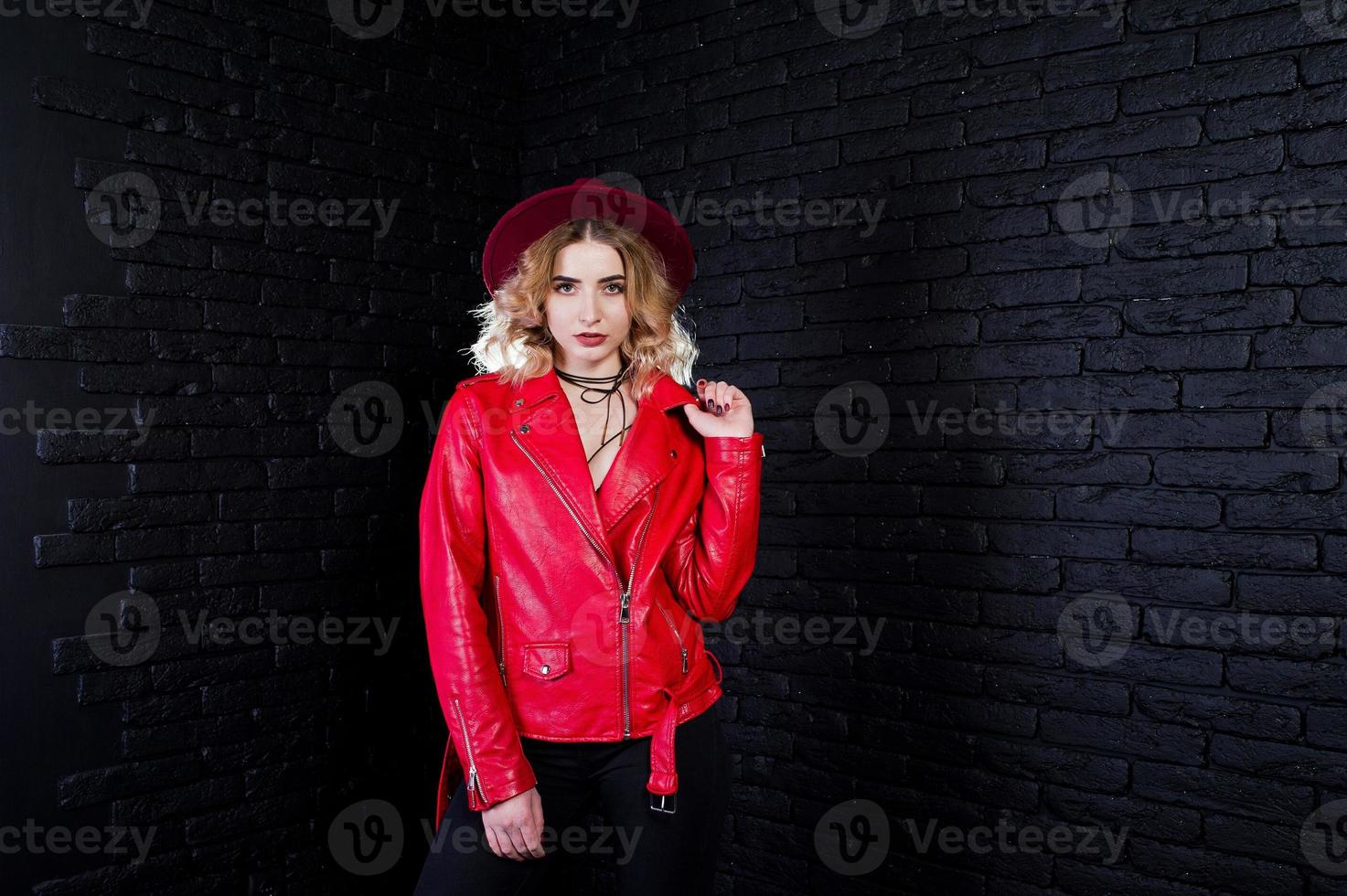 retrato de estudio de una chica rubia con sombrero rojo y chaqueta de cuero contra la pared de ladrillo. foto