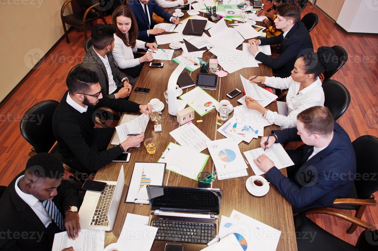 Multiracial business team addressing meeting around boardroom table, working together and write something on papers. photo