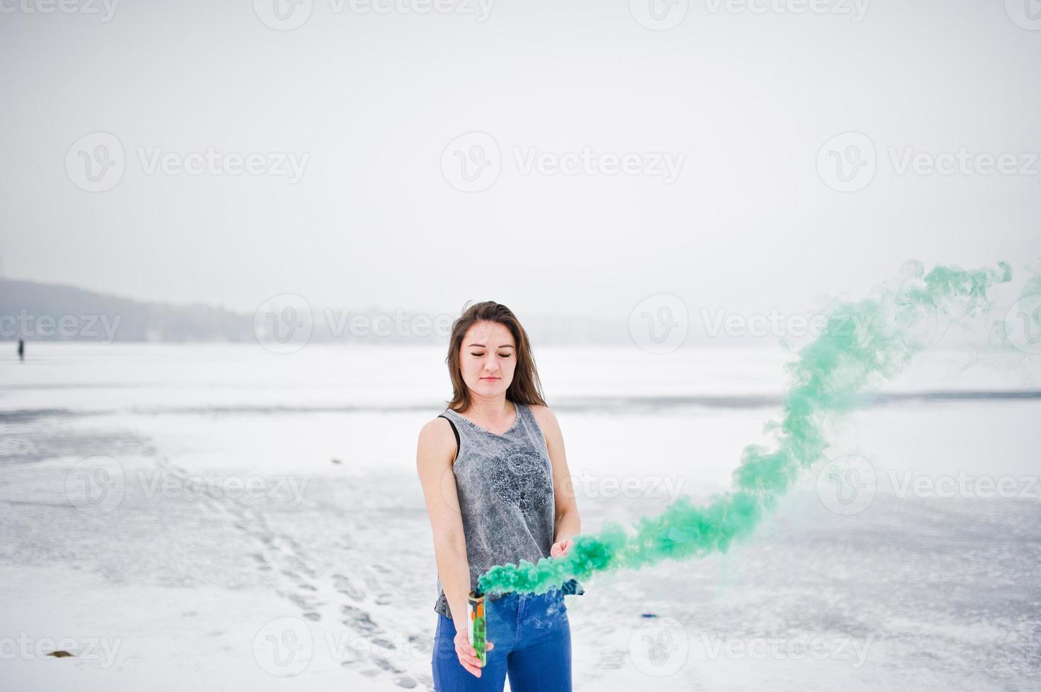 Young girl with green colored smoke bomb in hand in winter day. photo