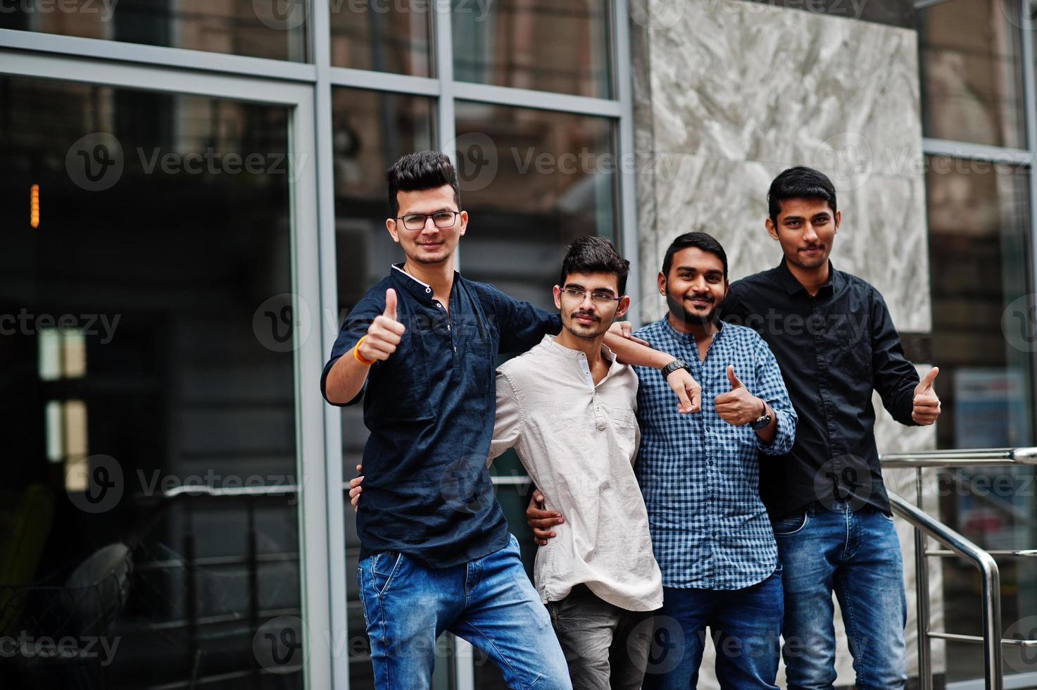 grupo de cuatro hombres indios, vestidos con ropa informal, posados al aire libre en la calle de la india. muestra el pulgar hacia arriba. foto