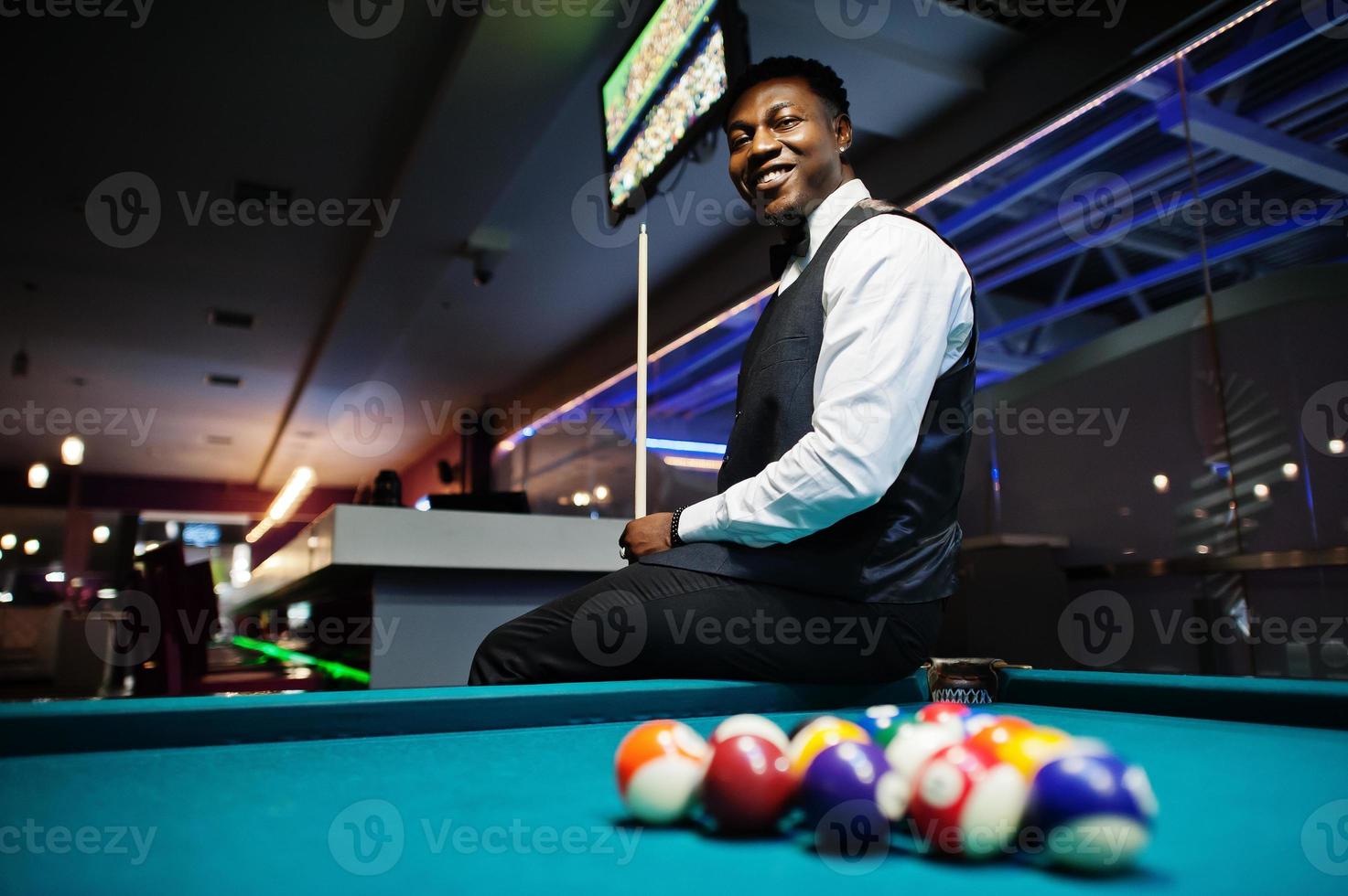 Young handsome african man wearing white shirt, black vest and bow tie play pool billiard. photo