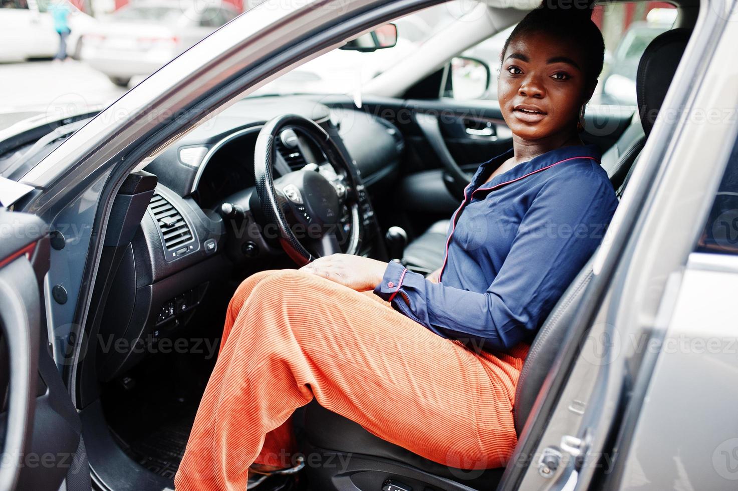 una rica mujer africana de negocios se sienta en el asiento del conductor en un camión todoterreno plateado con la puerta abierta. foto