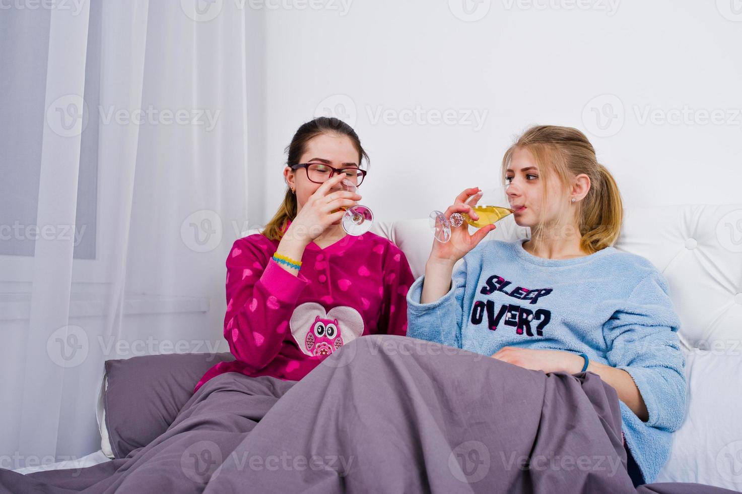 Two friends girls in pajamas having fun on bed at room. photo