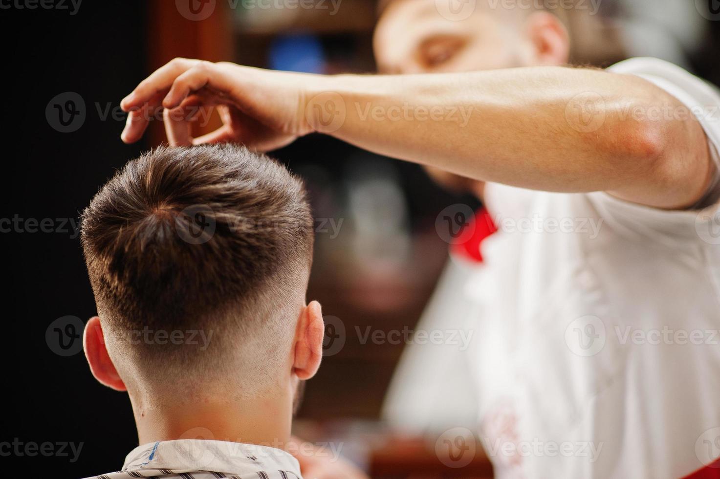 Young bearded man getting haircut by hairdresser while sitting in chair at barbershop. Barber soul. photo