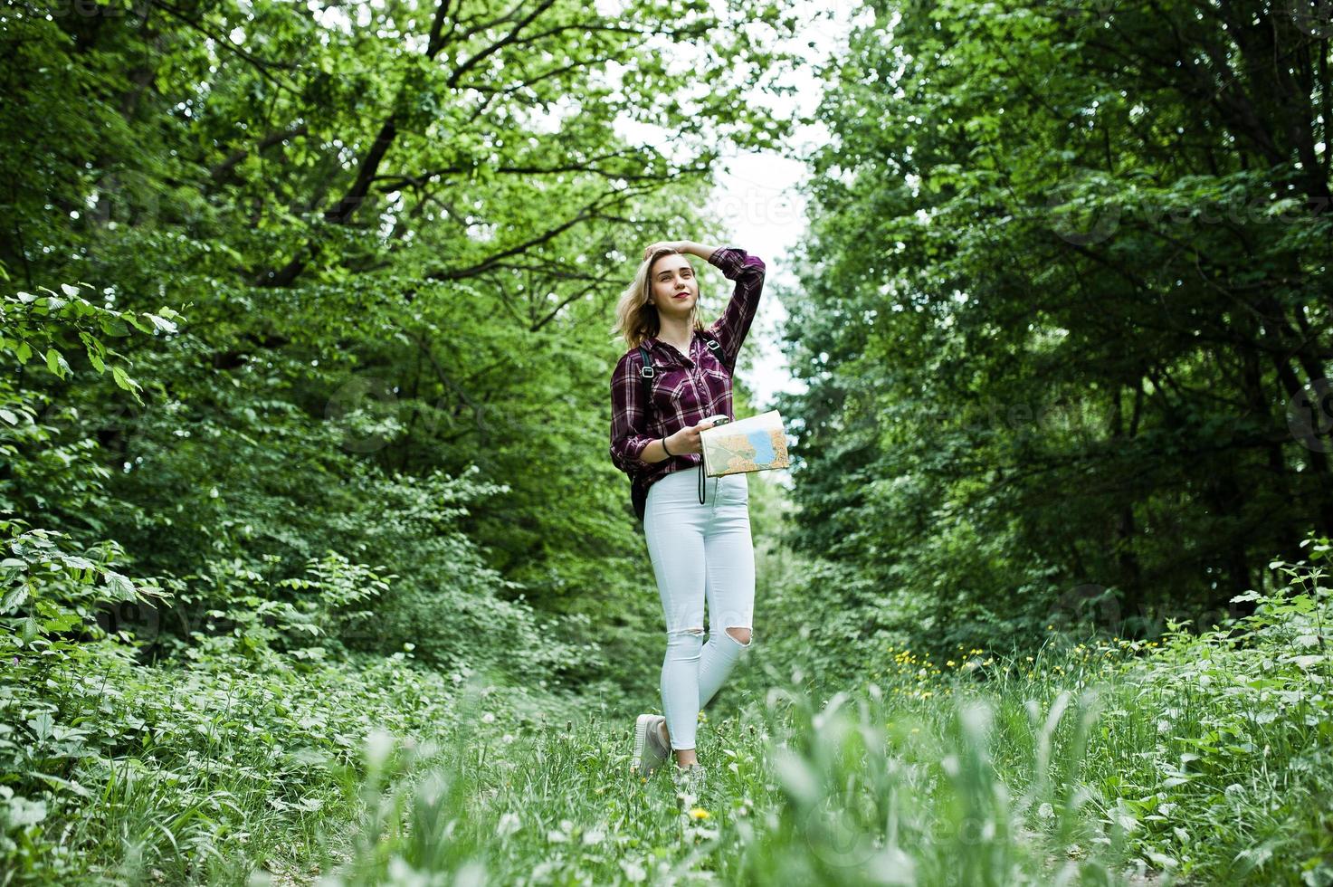 Portrait of a young beautiful blond woman in tartan shirt holding a map in the forest. photo