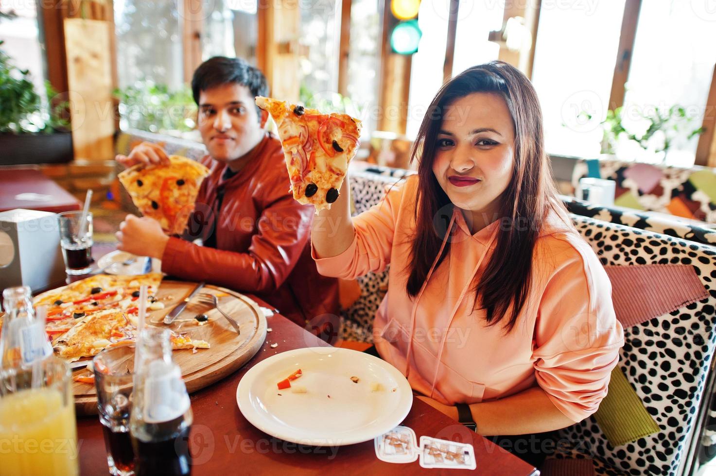 pareja de amigos asiáticos comiendo pizza durante la fiesta en la pizzería. gente india feliz divirtiéndose juntos, comiendo comida italiana y sentados en el sofá. foto