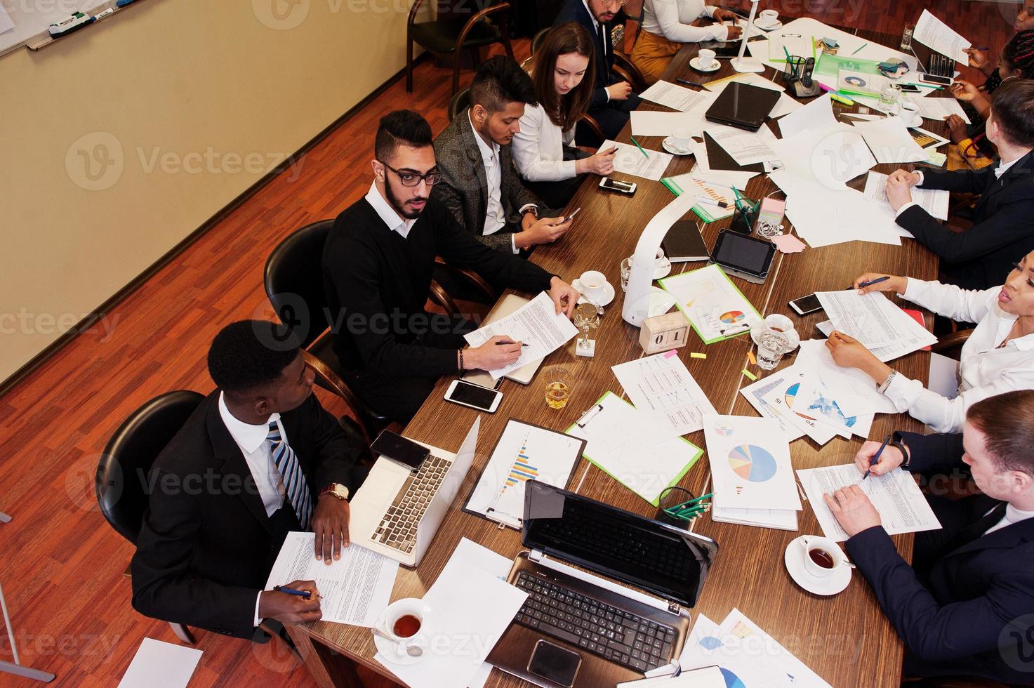 Multiracial business team addressing meeting around boardroom table, working together and write something on papers. photo