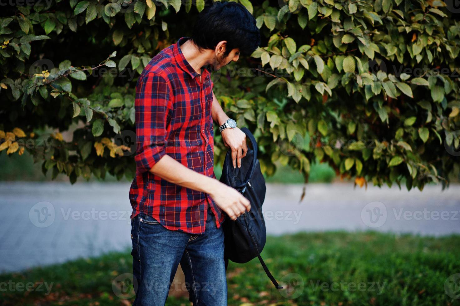 Young indian student man at red checkered shirt and jeans with backpack posed at street. photo