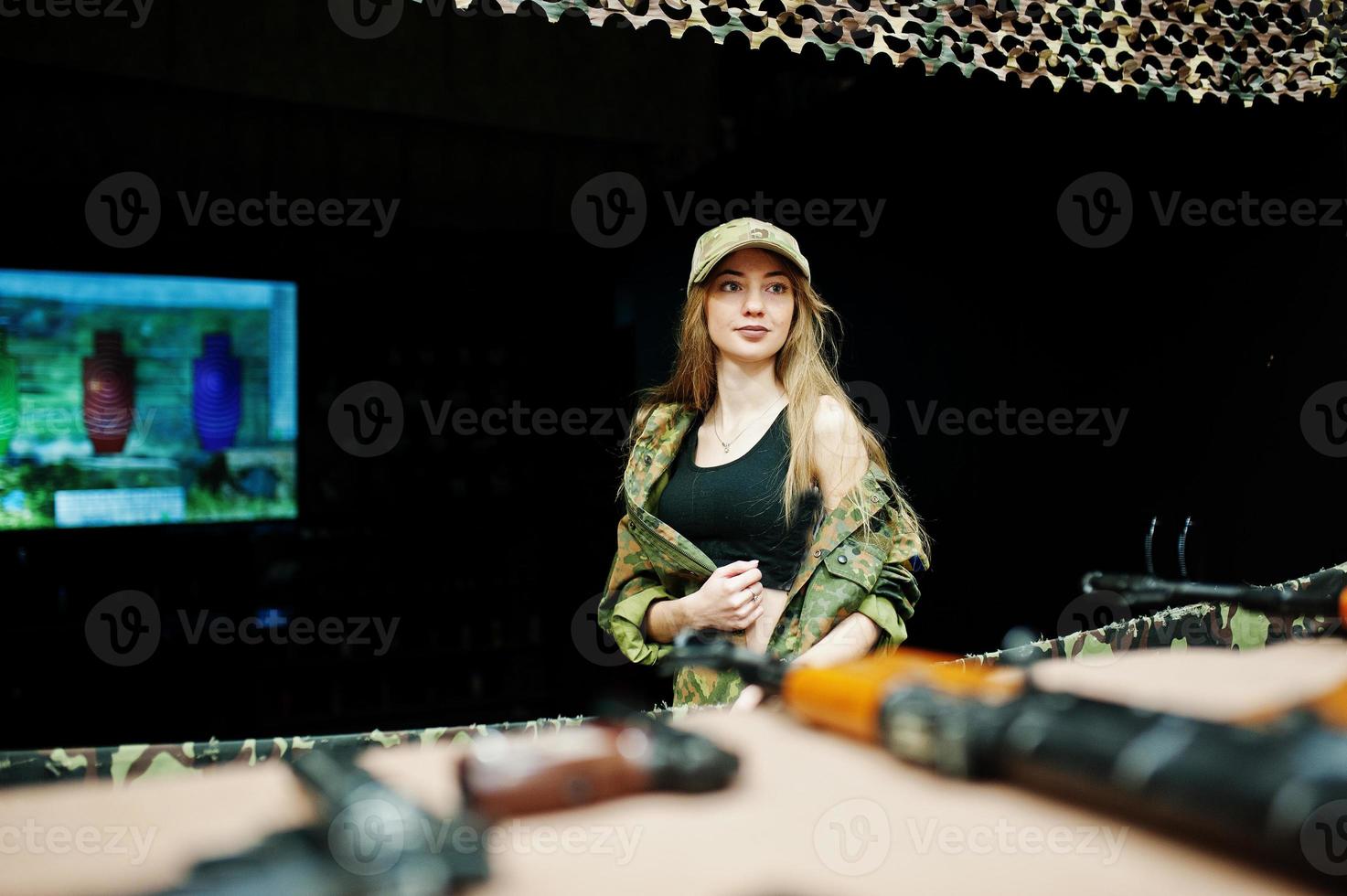 Military girl in camouflage uniform against army background on shooting range. photo