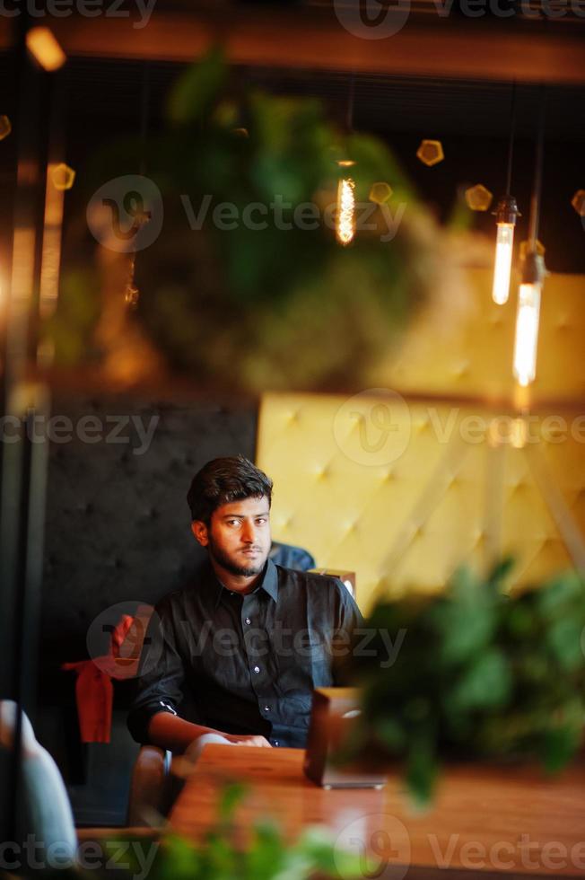 un joven indio confiado con camisa negra sentado en el café. foto