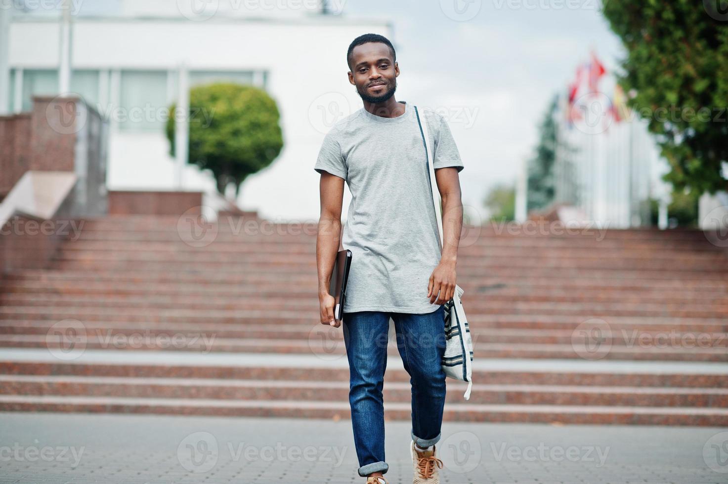 African student male posed with backpack and school items on yard of university, against flags of different countries. photo