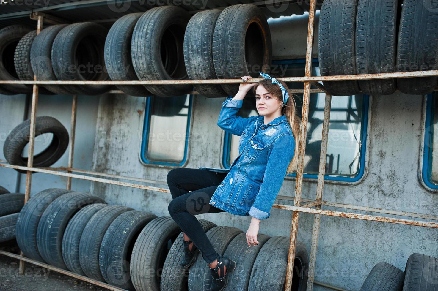 Young hipster girl in jeans jacket and head scarf at tire fitting zone. photo