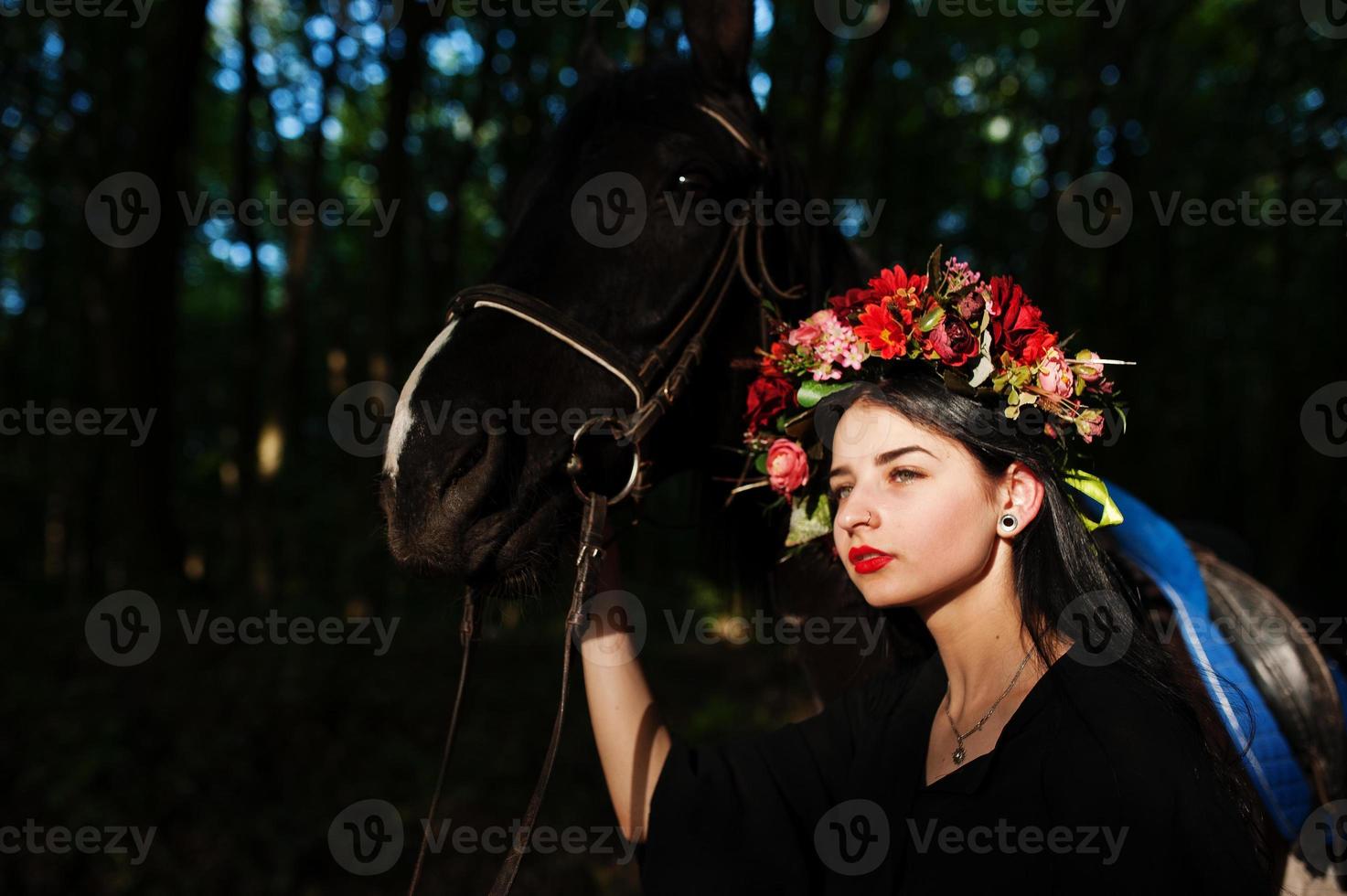 Mystical girl in wreath wear in black with horse in wood. photo