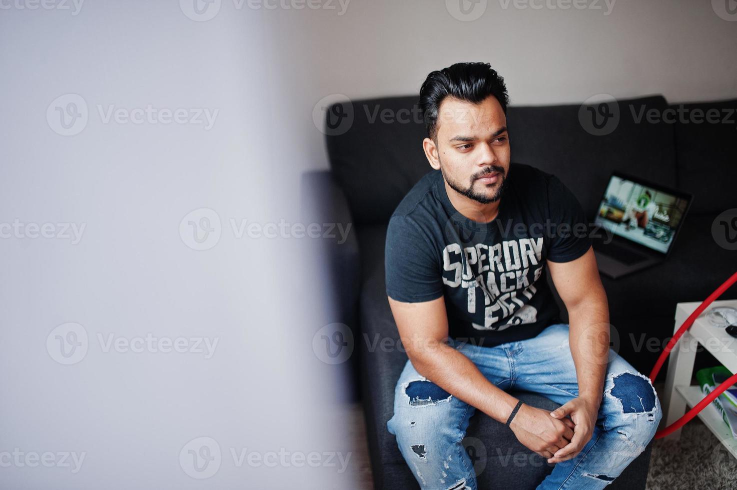 Casual beard indian man sitting at room against laptop. photo