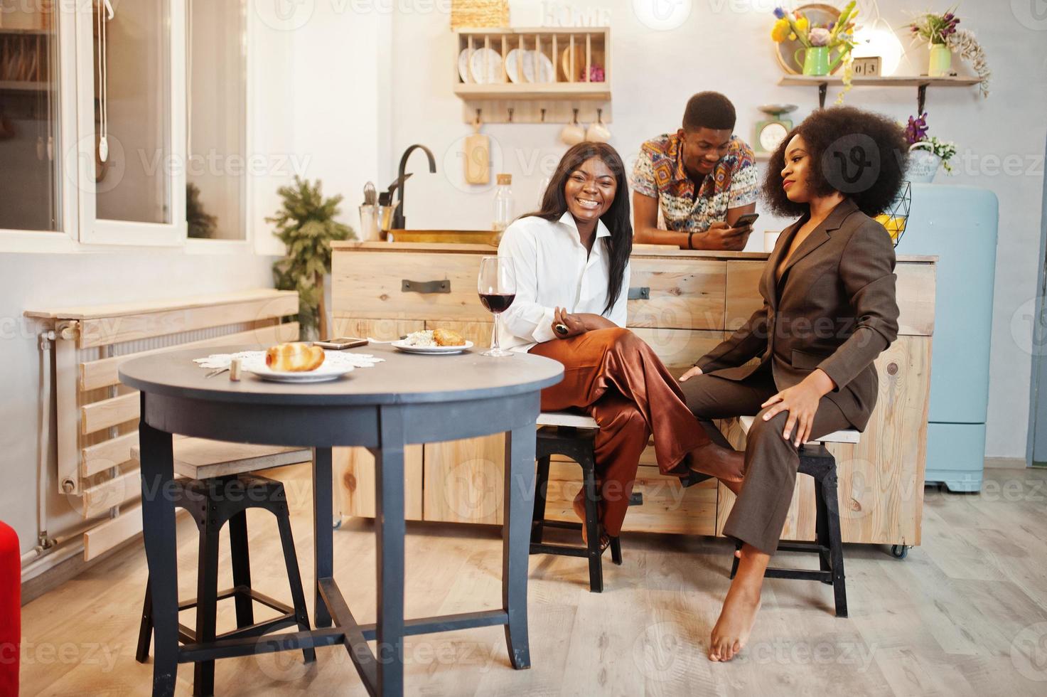 Three african american friends spending time at kitchen with wine. Black peoples relaxing at home. photo