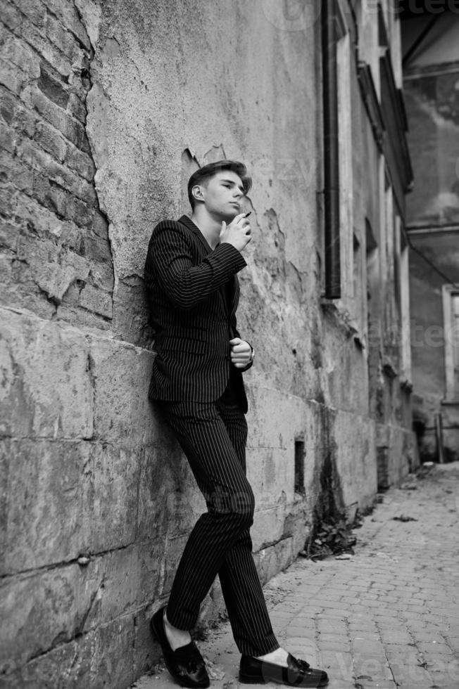 Young macho boy wear on blac stylish jacket smoking cigarette on streets. photo