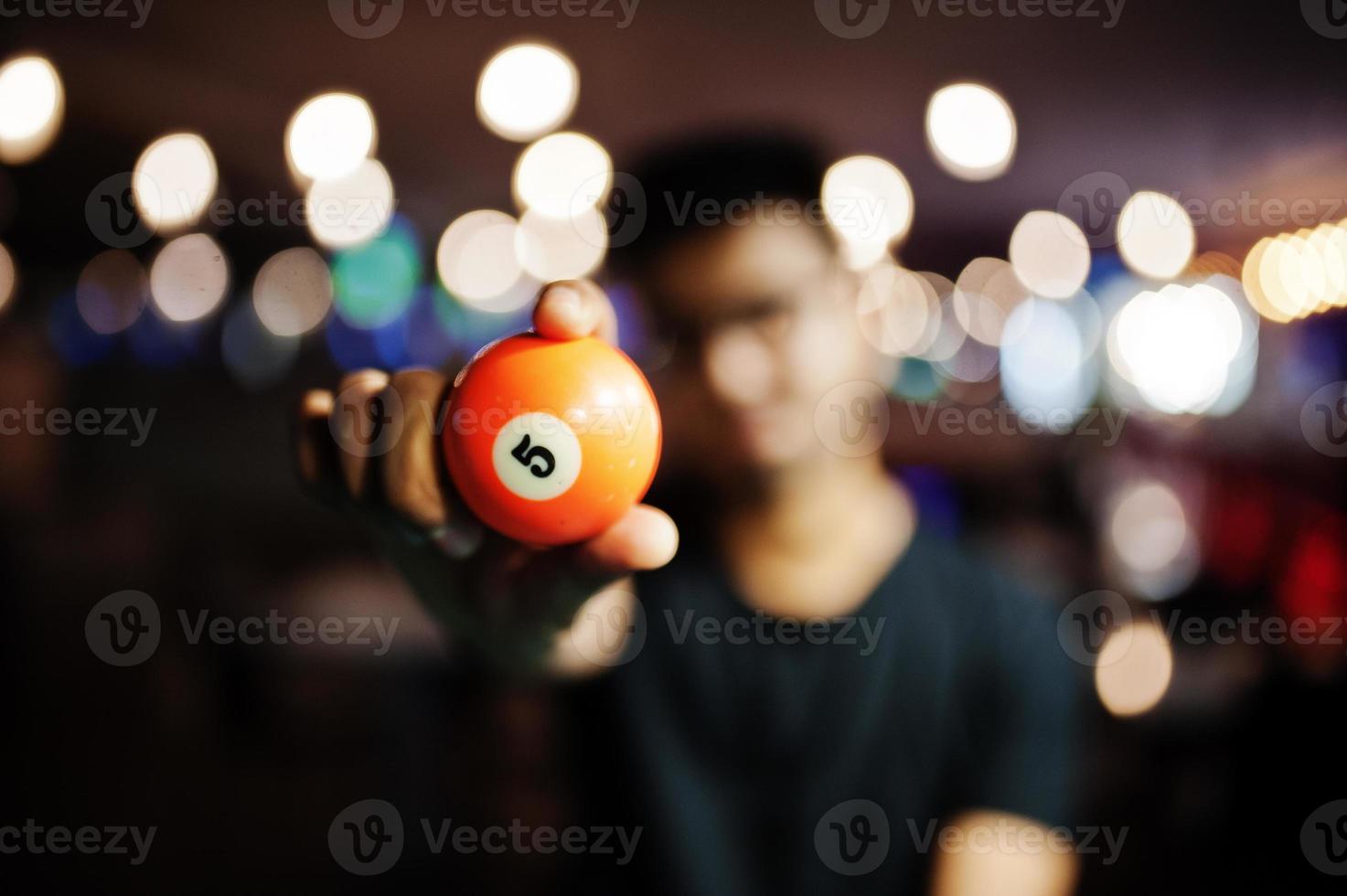 Orange pool ball with 5 hold at hands man. Blured background. Billiard theme. photo