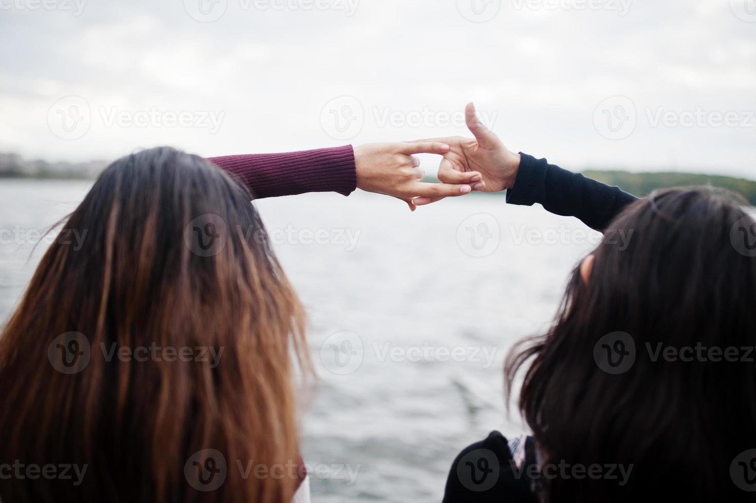 Portrait of back two young beautiful indian or south asian teenage girls in dress show  joined hands. photo