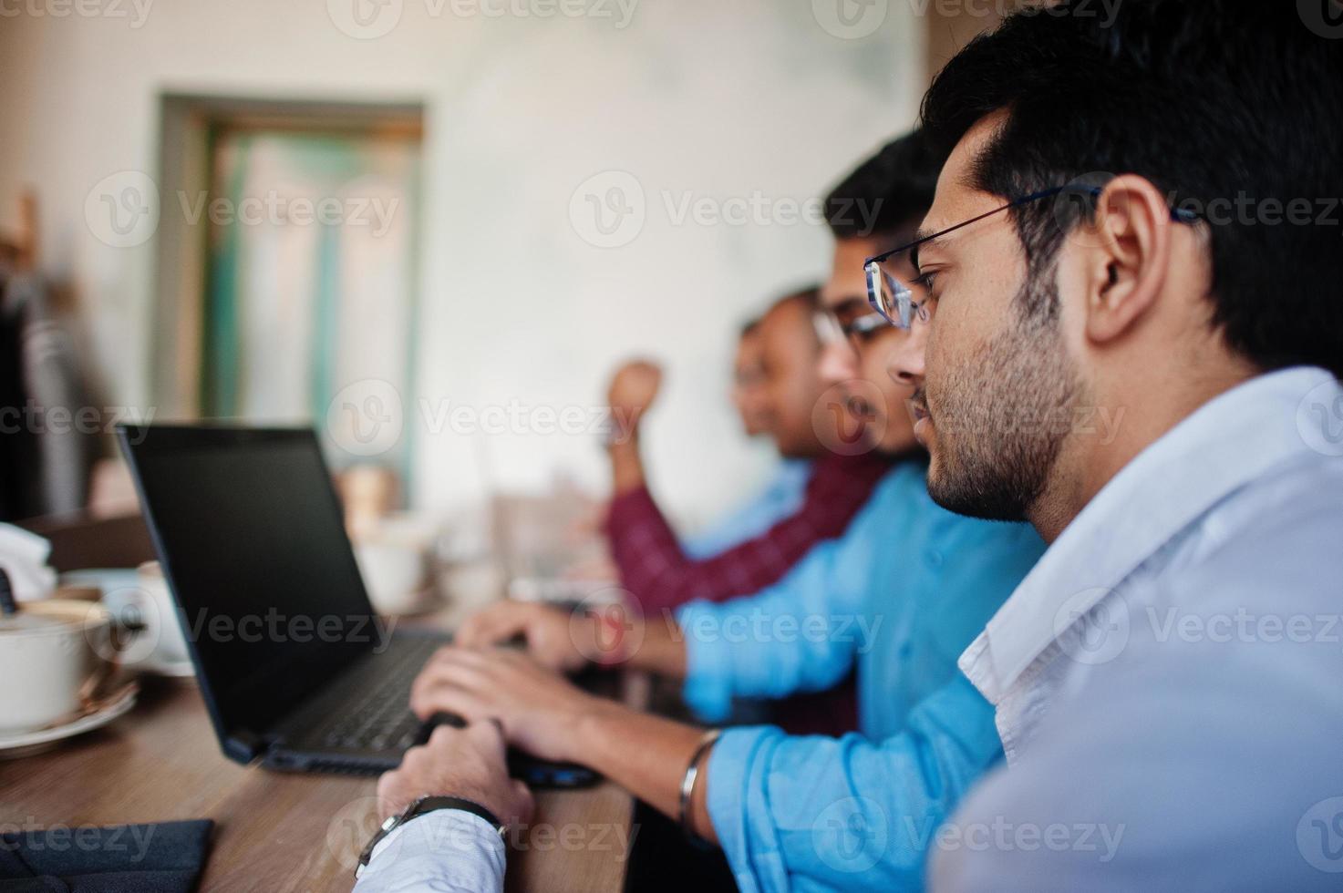 Group of four south asian men's posed at business meeting in cafe. Indians work with laptops together using various gadgets, having conversation. photo