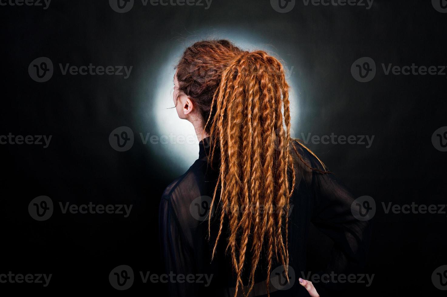 Studio shoot back of girl in black with dreads at black background with nimbus. photo