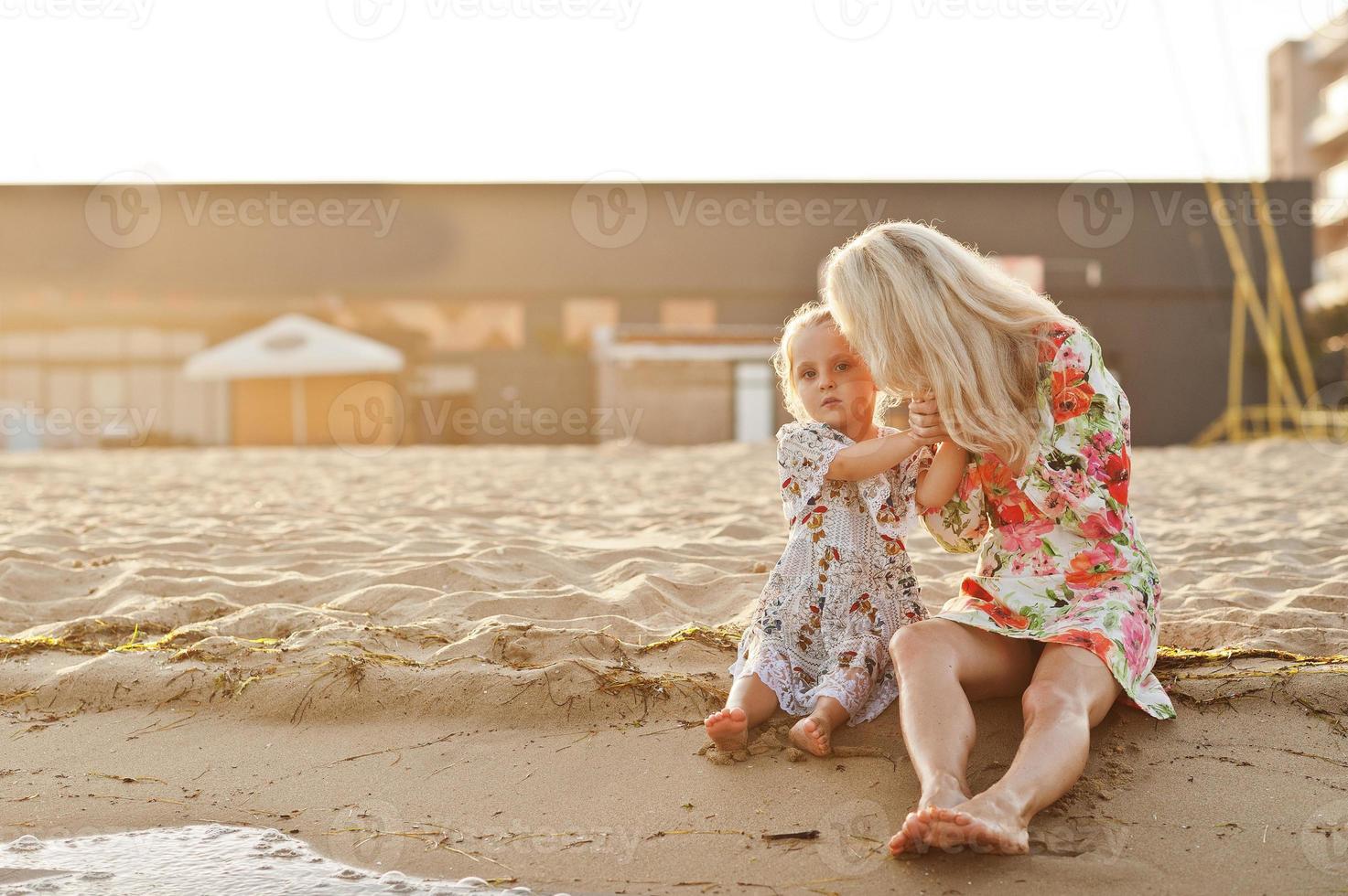 Mother and beautiful daughter having fun on the beach. Portrait of happy woman with cute little girl on vacation. photo