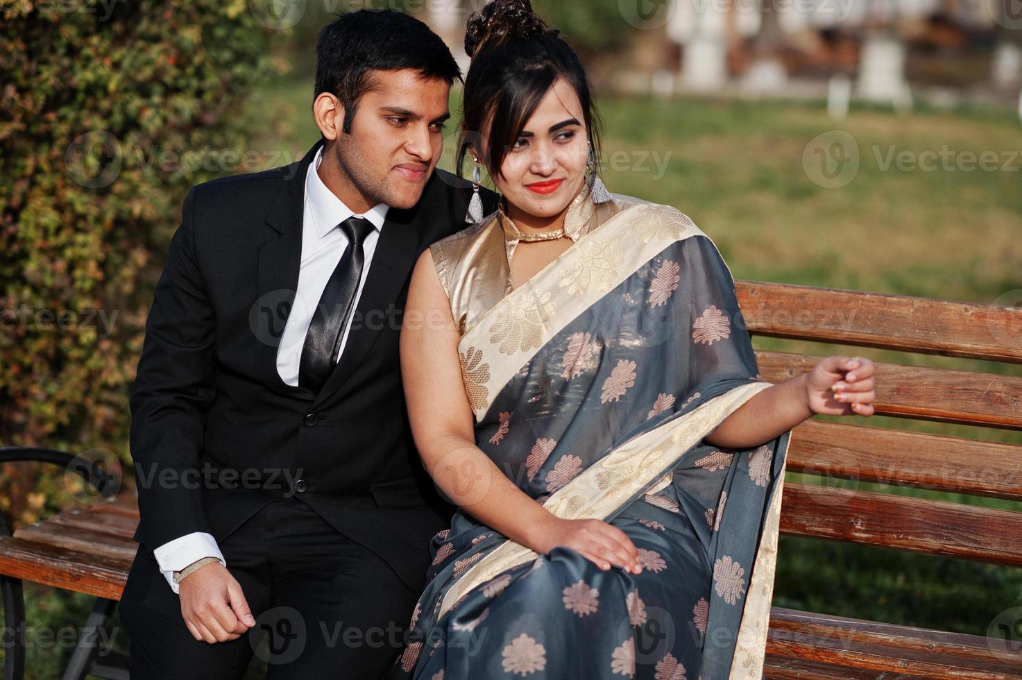 Elegant and fashionable indian friends couple of woman in saree and man in suit sitting on bench. photo