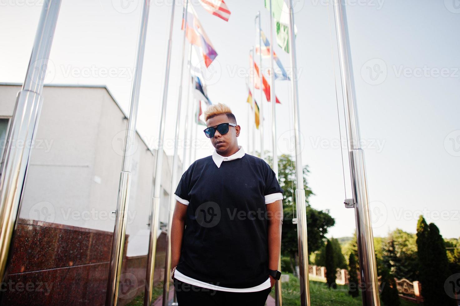 Stylish arabian muslim boy with originally hair posed on streets, against flags of different countries. photo