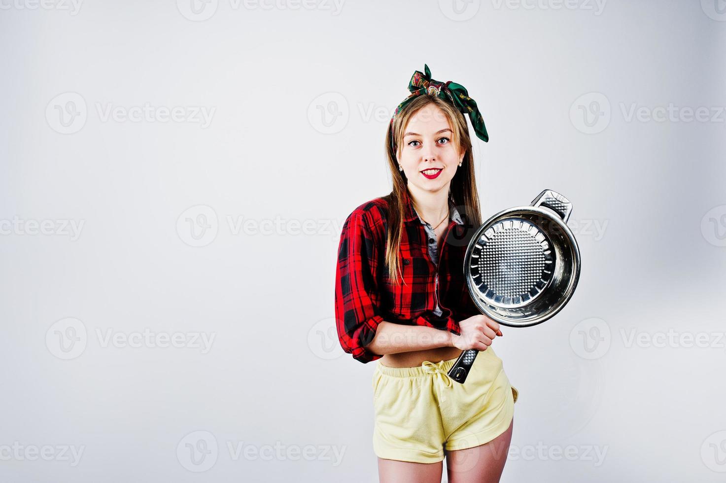 Young funny housewife in checkered shirt and yellow shorts pin up style with frying pan isolated on white background. photo