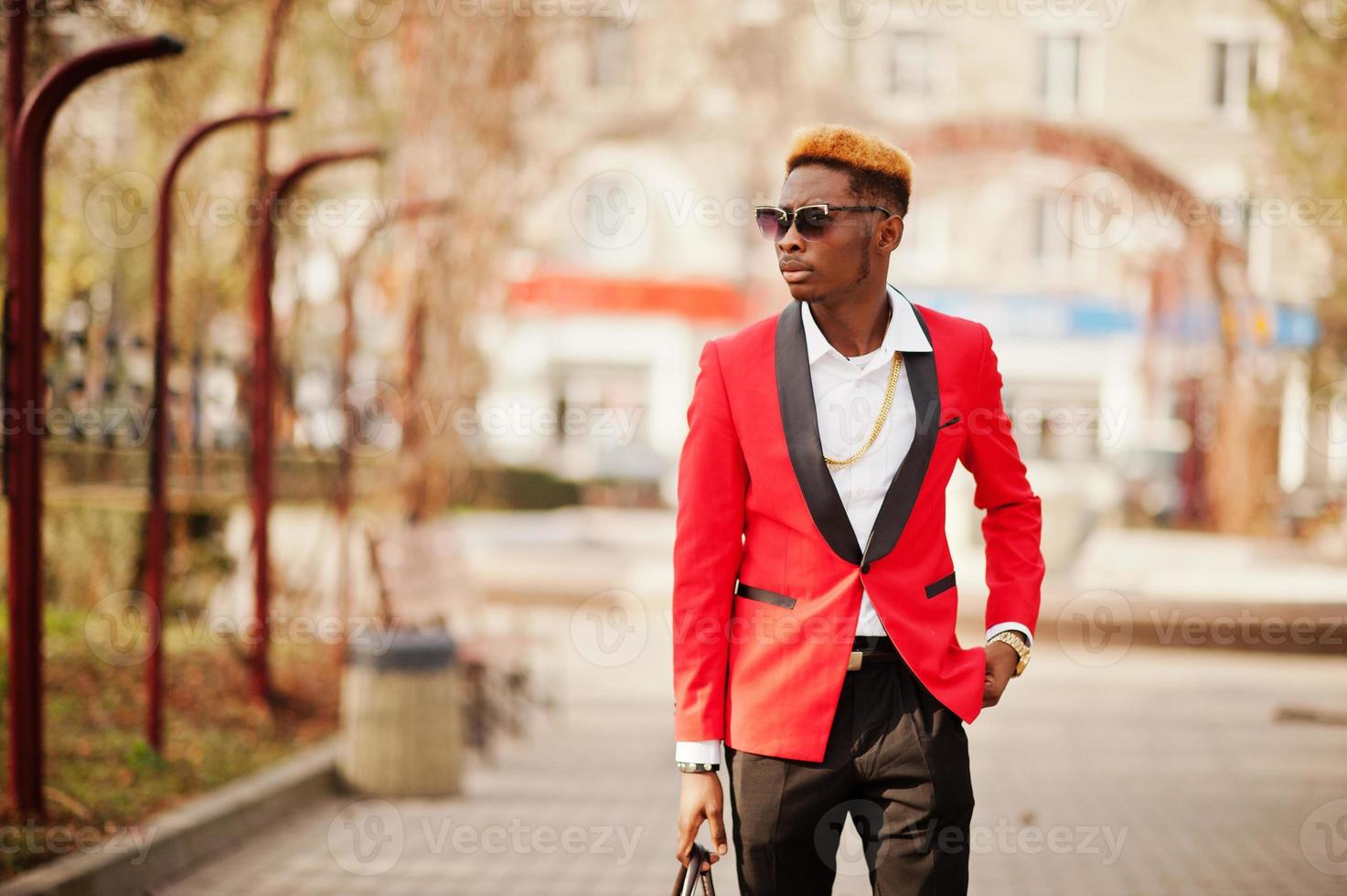 Fashion african american man model at red suit, with highlights hair and handbag posed at street. photo