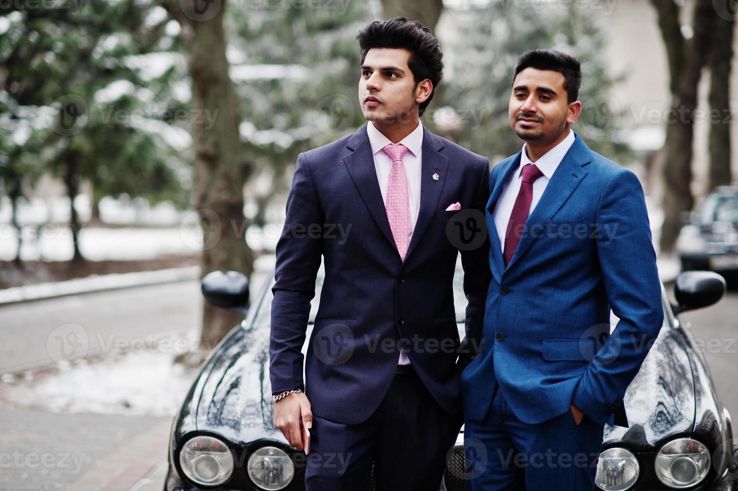dos elegantes modelos indios de moda en traje posaron en el día de invierno contra un auto clásico negro. foto