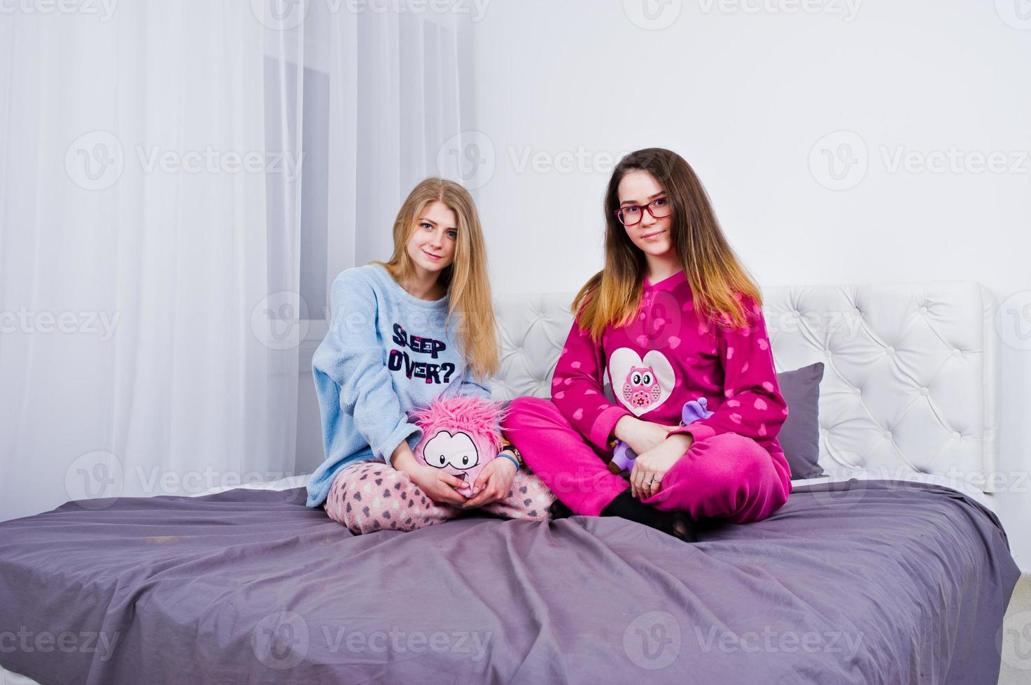 Two friends girls in pajamas having fun on bed at room. photo